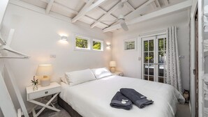 Un dormitorio con una cama, dos mesitas de noche con lámparas, un ventilador de techo y vistas al exterior a través de una puerta.