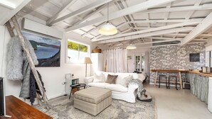 Una sala acogedora con un sofá blanco, un pequeño reposapiés y un cuadro de un paisaje marino.
