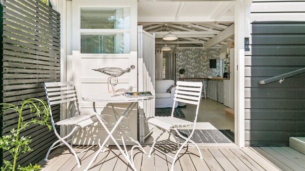 Un patio con una mesa, dos sillas, una escultura decorativa de pájaro y vistas hacia la casa.