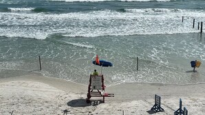 A lifeguard station with a red and white sign, a blue umbrella, and a beach chair.