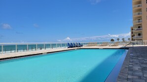 A clear blue pool with lounge chairs and a view of the ocean.
