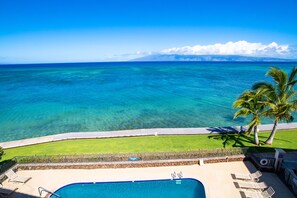 Relax by the oceanfront pool surrounded by lush greenery and a distant mountain range.