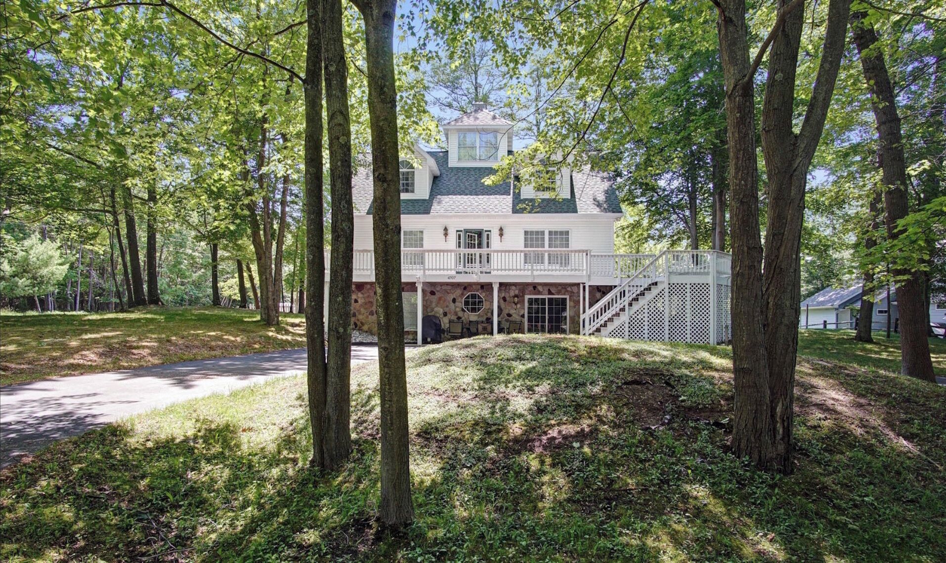 A large, two-story house with a stone foundation, a covered porch, and a staircase leading to a second-floor balcony.