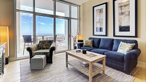 A living room with a large window, a sofa, a chair, and a coffee table. - Emerald By the Sea #813, Beautiful Gulf View, Luxury Hi Rise 2 Bedroom Condo (Galveston)