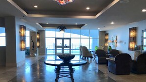 A spacious lobby with a round table and chairs, large windows, and modern lighting fixtures. - Emerald By the Sea #813, Beautiful Gulf View, Luxury Hi Rise 2 Bedroom Condo (Galveston)