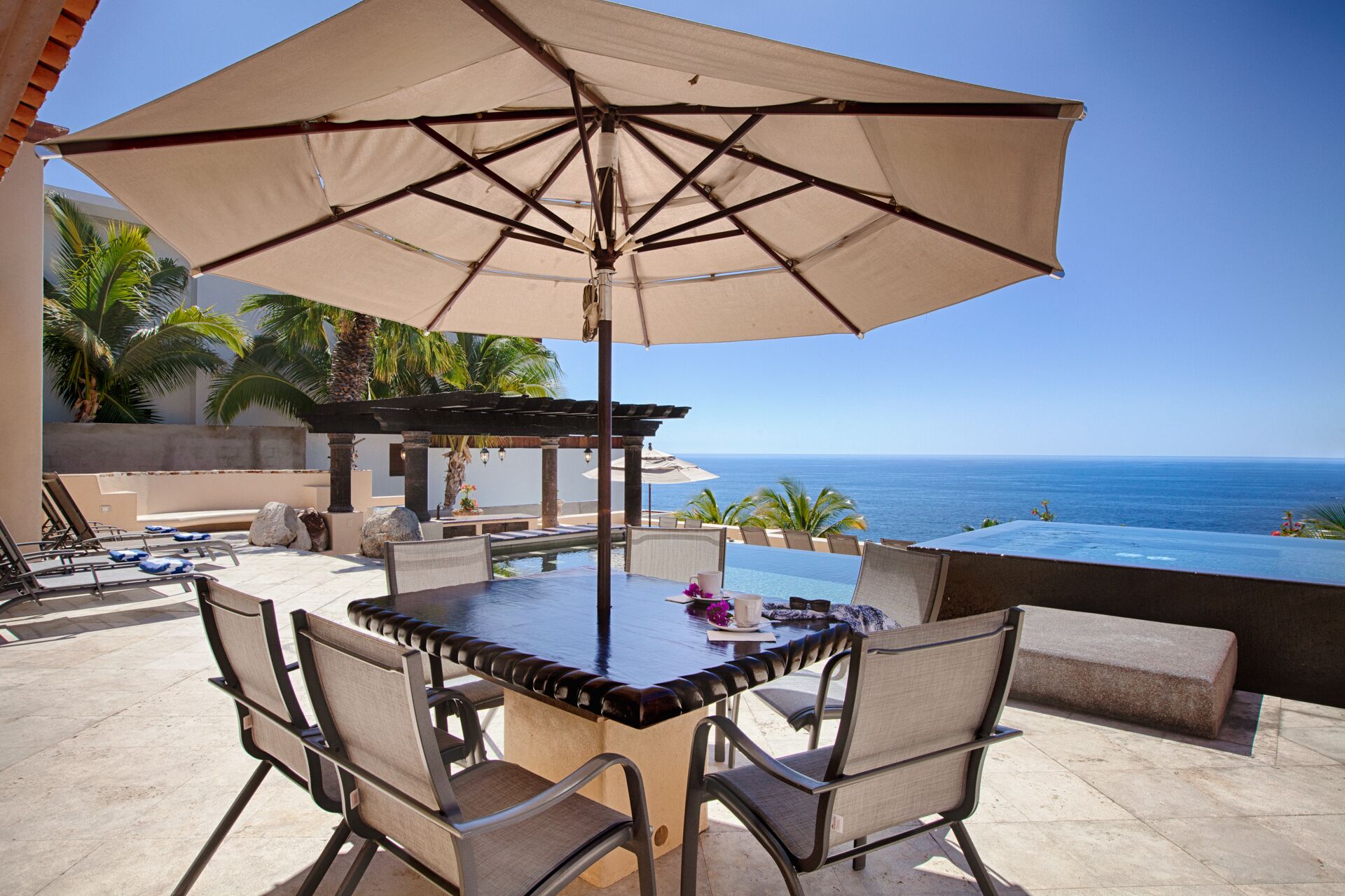 An outdoor dining area with a pool, overlooking the ocean.