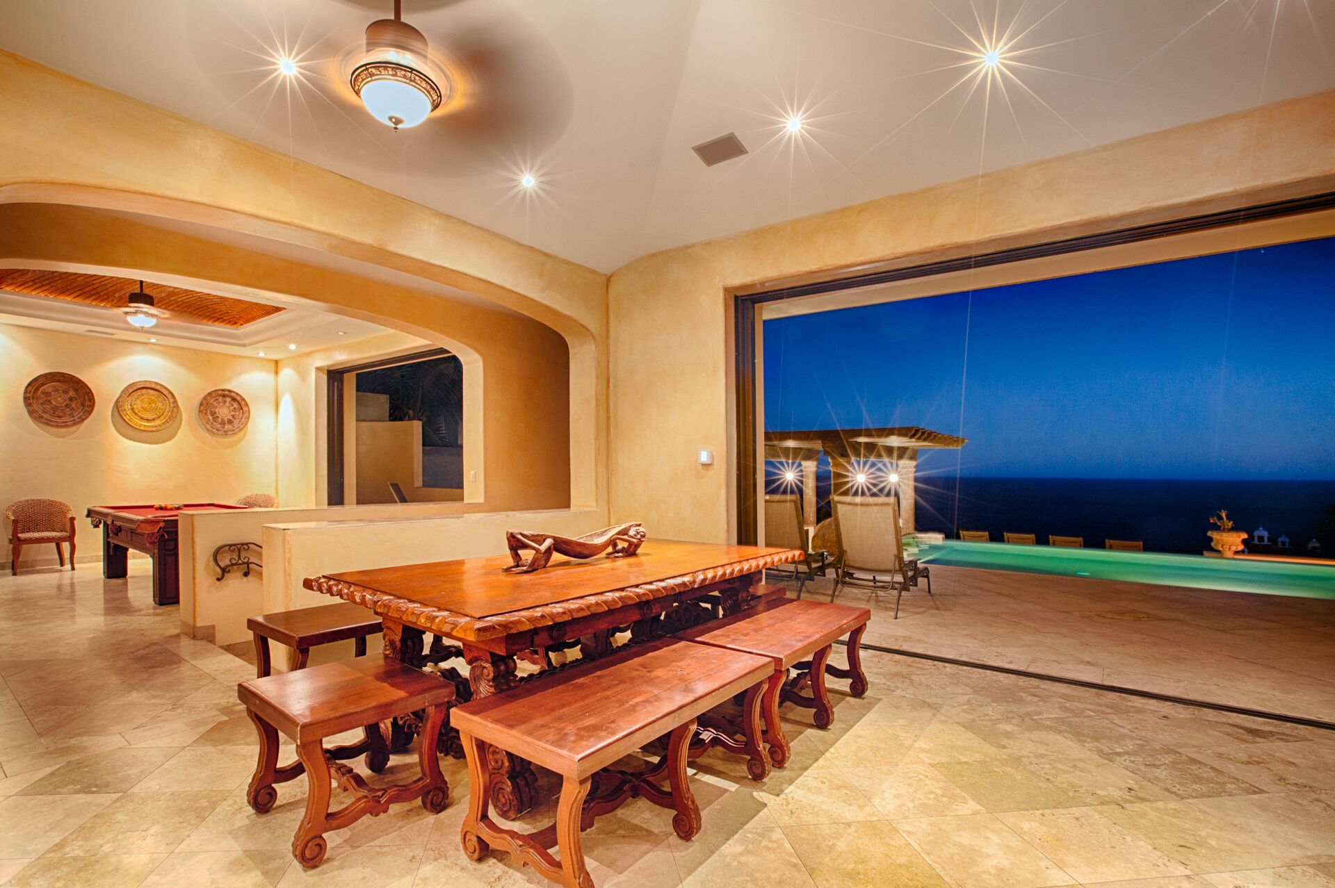 A spacious indoor area with a poolside view, a pool table, and a dining table with benches.