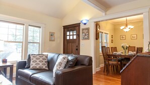 A living room with a brown leather sofa, a dining table with chairs, and a chandelier. - Green Gables-2 Fireplaces,Salt Hot tub, 100+mbps Wifi, AC, Bikes, Big Yard,Walk! (Bend)