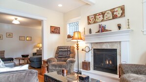 A living room with a fireplace, a glass coffee table, and a blue armchair. - Green Gables-2 Fireplaces,Salt Hot tub, 100+mbps Wifi, AC, Bikes, Big Yard,Walk! (Bend)