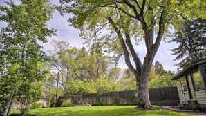 A residential backyard with a well-maintained lawn, a large tree, a wooden fence, and a house with a front porch. - Green Gables-2 Fireplaces,Salt Hot tub, 100+mbps Wifi, AC, Bikes, Big Yard,Walk! (Bend)