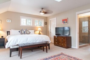 A bedroom with a bed, bedside lamps, a TV, a bench, a dresser, and a shower area.