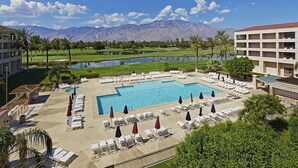 A resort pool area with multiple lounge chairs and umbrellas, a large central pool, and a view of mountains and a golf course in the background. - Desert Princess Cc And Resort, On Golf Course, W/ Mountain Views (Cathedral City)