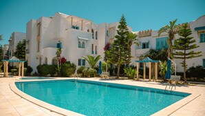 A swimming pool with a tiled deck, surrounded by white buildings with blue accents and palm trees. - Beautiful view apartment located at Yasmine Hammamet with garden, swimming pool  (Yasmine hammamet)