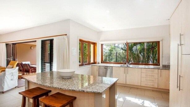 Una cocina moderna con encimera de granito, taburetes de madera y vistas al exterior.