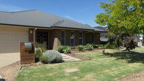 A residential house with a brick facade, a grey roof, and a well-maintained lawn with various plants. - Parkins Fairway - Golf, Lake & Relaxation (Yarrawonga)