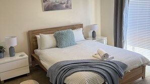A bedroom with a wooden bed, a ceiling fan, a nightstand with a lamp, a bedside table, and a window with curtains. - Parkins Fairway - Golf, Lake & Relaxation (Yarrawonga)