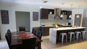 A modern kitchen with a central island, bar stools, and a dining area with a wooden table and chairs. - Parkins Fairway - Golf, Lake & Relaxation (Yarrawonga)