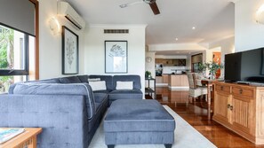 A modern living room with a grey sectional sofa, a wooden cabinet, and a television. - 5 The Point Apartments  |  Port Douglas (PORT DOUGLAS)