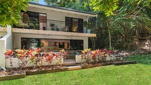 Ein modernes, zweistöckiges Haus mit Balkon, umgeben von üppiger Bepflanzung und einem gepflegten Garten.