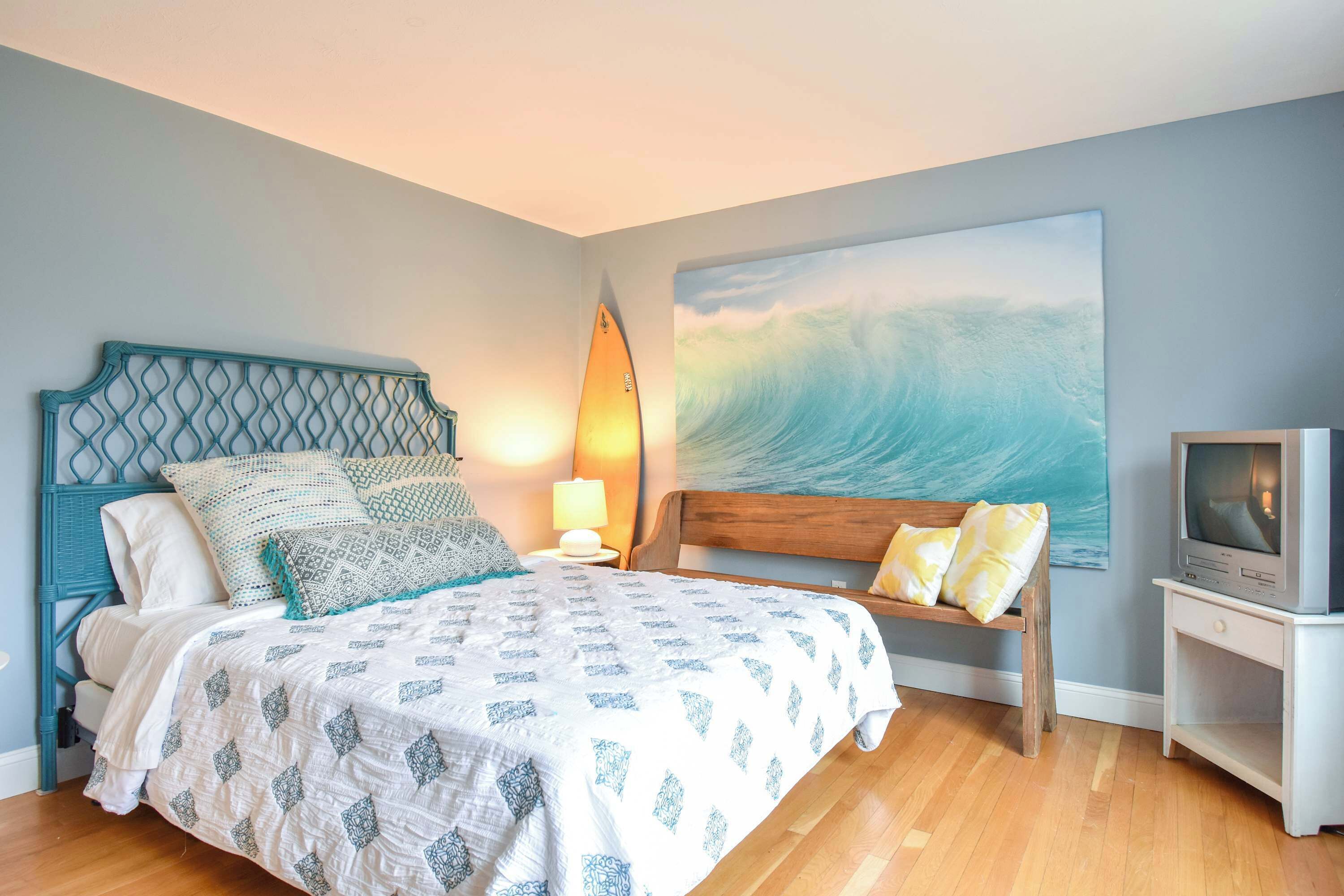 A bedroom with a bed, a nightstand, a TV, and a large wave painting on the wall.