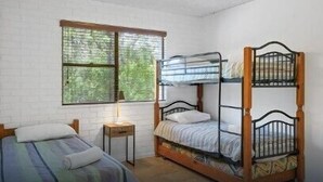A room with a bunk bed, a single bed, a small table, and a window with a view of trees. - 2/56 Lawson Street at Clarkes Beach (Byron Shire)