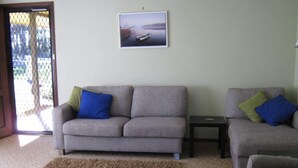 A living room with two grey sofas, one with blue and green cushions, and a small table. A framed picture hangs on the wall.