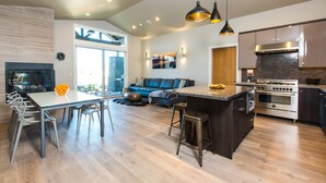 A modern kitchen with a central island, a dining area with a white table and chairs, and a living space with a blue sofa and a fireplace. - Plush beds ~ heated resort pool ~ hot tub ~ Tetherow/Bend/Bachelor ~ wifi ~ 🐶 (Bend)
