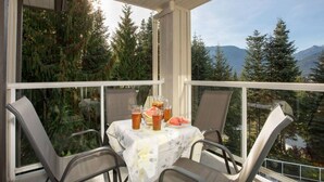 A balcony with a table set for two, featuring a pitcher of iced tea, a watermelon, and a glass of beer. - Mountain-Side 3Br/2Ba - HotTub/Views/Free Parking (Whistler)