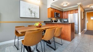 A modern kitchen with wooden cabinets, a central island, and a dining area with a wooden table and chairs. - Mountain-Side 3Br/2Ba - HotTub/Views/Free Parking (Whistler)