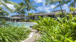 Relax by the serene pool surrounded by lush tropical vegetation and modern buildings.