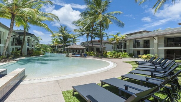 A resort pool area with lounge chairs, palm trees, and resort buildings. - Azure 125-126 | Port Douglas (PORT DOUGLAS)