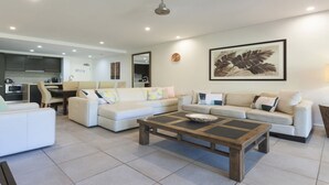 A modern living room with a sectional sofa, a coffee table, and a kitchen in the background. - Azure 125-126 | Port Douglas (PORT DOUGLAS)
