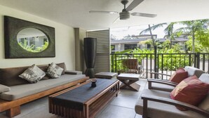 A modern living room with a sofa, coffee table, and chairs, a ceiling fan, and a view of a lush garden. - Azure 125-126 | Port Douglas (PORT DOUGLAS)