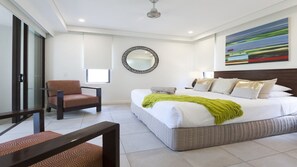 A modern bedroom with a large bed, a chair, a mirror, and a painting on the wall.