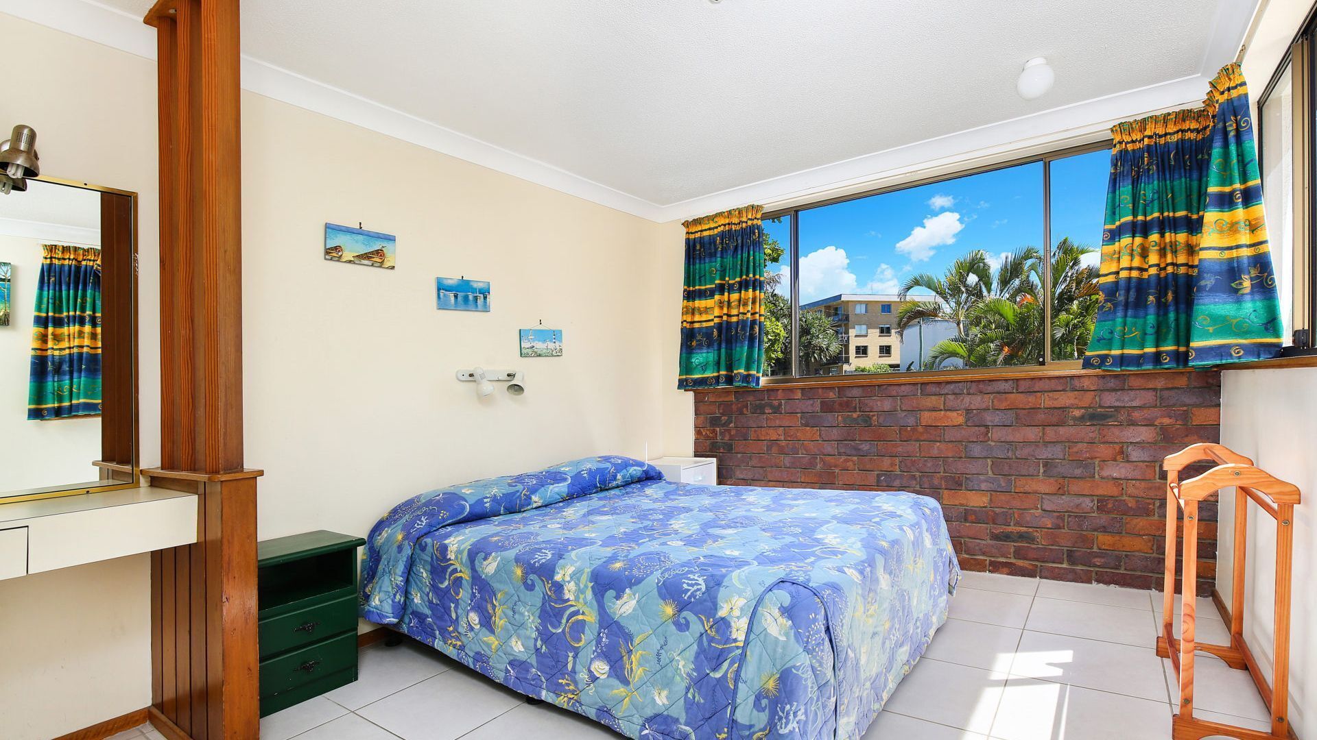 Un dormitorio con cama, cómoda, espejo y ventana con cortinas.