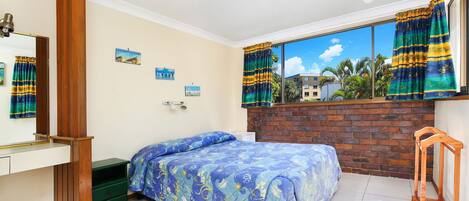 Un dormitorio con cama, cómoda, espejo y ventana con cortinas.