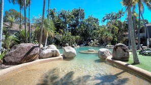Relax by the resort pool surrounded by lush tropical vegetation and large rocks.
