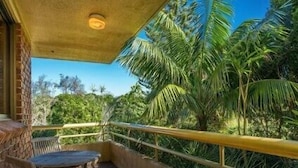 A balcony with a table and chairs, surrounded by lush greenery and palm trees. - Breeze at Byron 1 Clarkes Beach (Byron Shire)