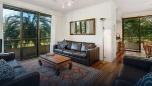 A spacious living room with a large sliding glass door leading to a balcony, a dark leather sofa, a wooden coffee table, and a floor lamp. - Breeze at Byron 1 Clarkes Beach (Byron Shire)