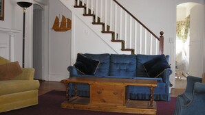Ein Wohnzimmer mit einem blauen Sofa, einem gelben Sessel, einem Holztisch und einer Treppe mit weißen Geländern.