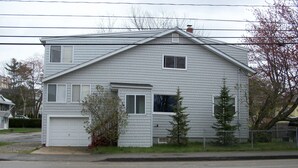 Ein zweistöckiges Haus mit Garage, kleiner Veranda und Vorgarten mit Baum und Zaun.