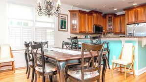 Un coin repas avec une table et des chaises en bois, un lustre, des meubles de rangement en bois et une cuisine équipée.