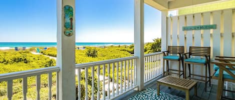 A balcony with a view of the beach, a sign reading 'Beach House', and outdoor furniture.