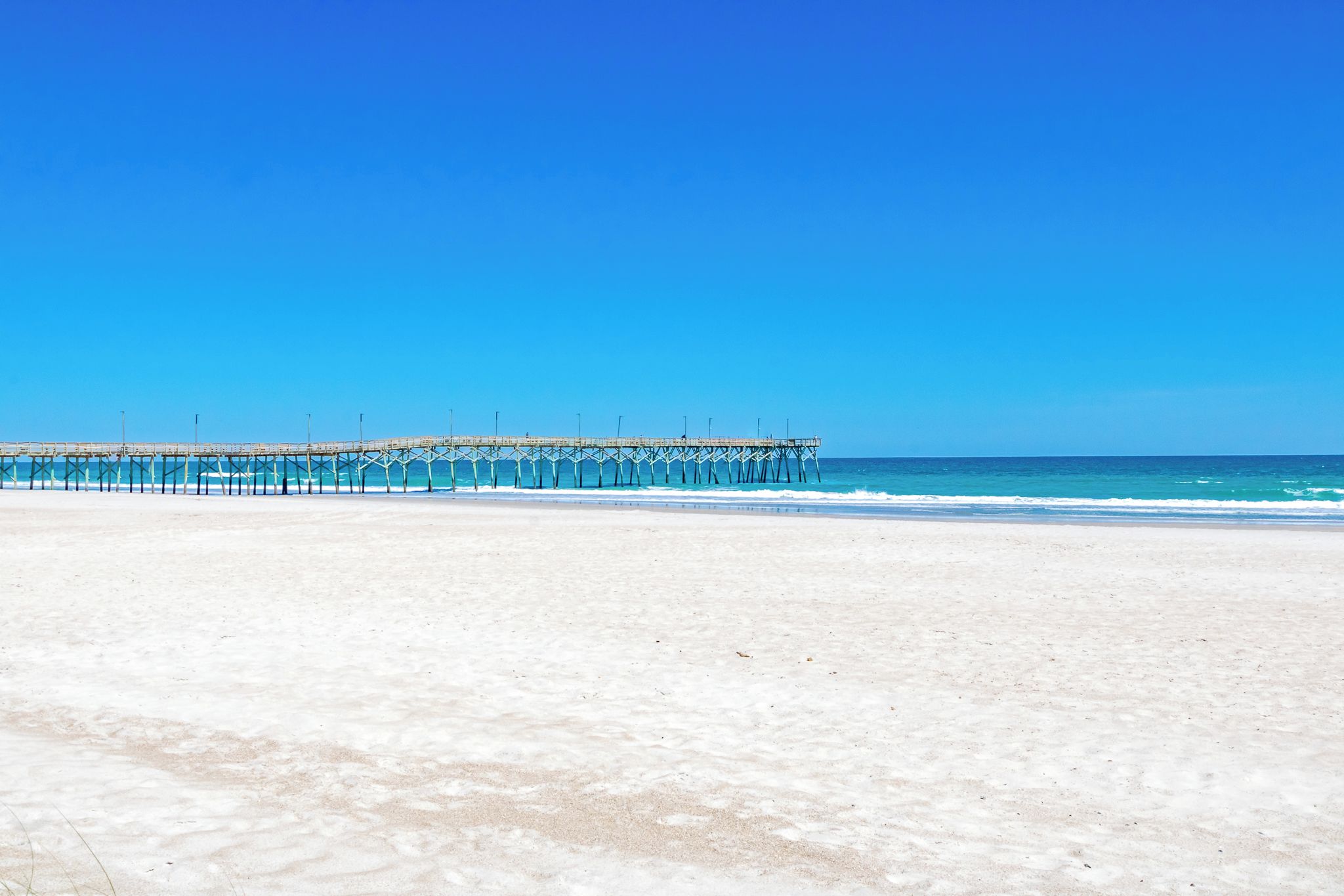 A beach with a pier extending into the ocean.