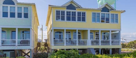A coastal house with a water tower, two-story structure, and a wooden walkway leading to the entrance.
