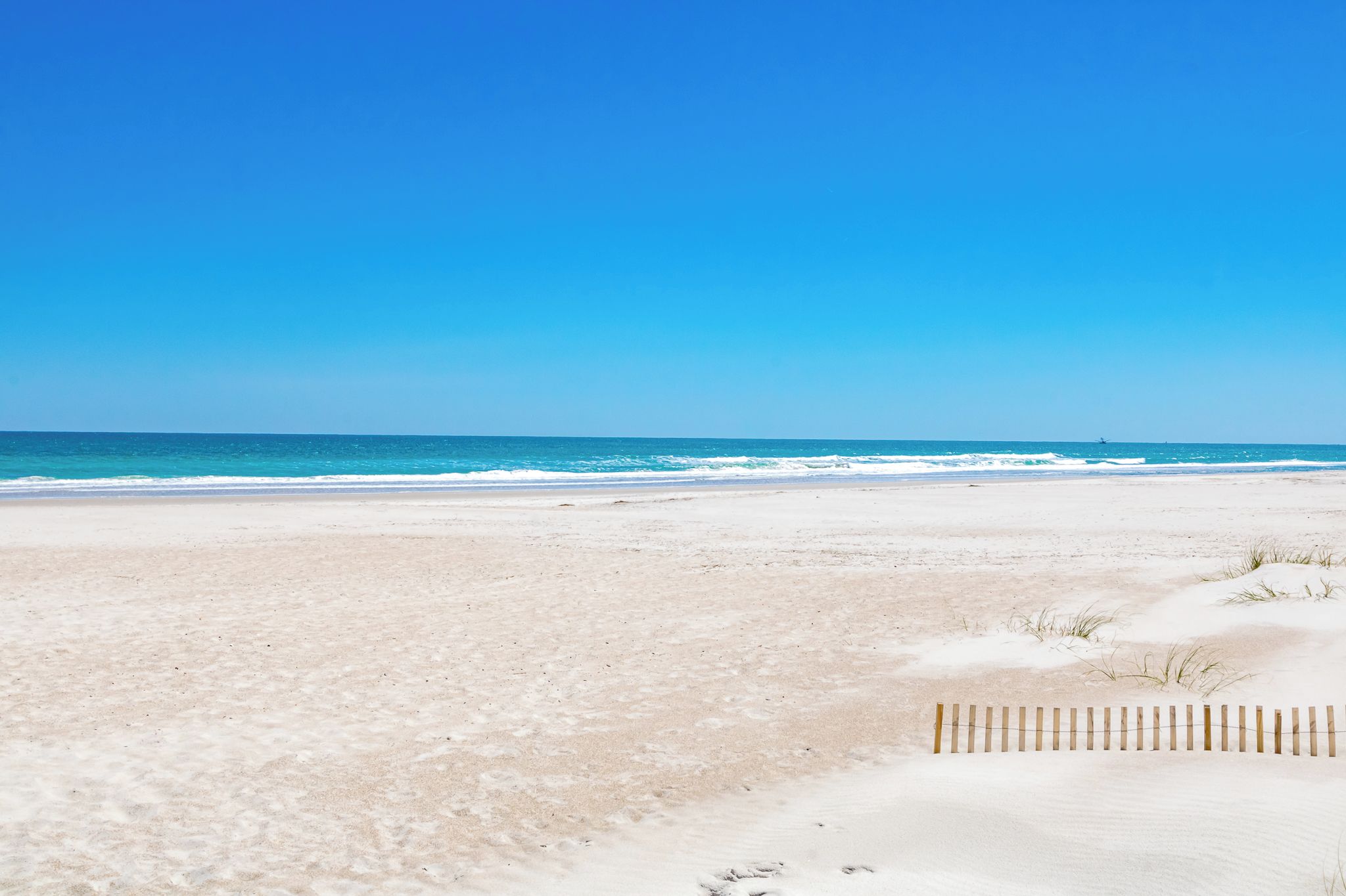 A beach with a wooden fence in the foreground and a clear blue sky.