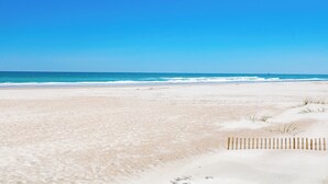 Une plage avec une clôture en bois au premier plan et un ciel bleu dégagé.