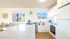 A modern kitchen with white cabinets, a large island, a dishwasher, and a refrigerator. - Intrepid, 15 3 Intrepid Close - right on the beachfront and WiFi (Nelson Bay)