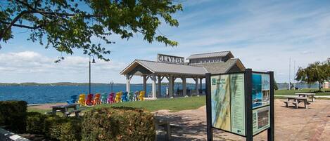 A pavilion with a sign reading "Clayton" by a lake, colorful chairs, and a picnic area.