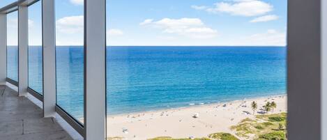 A balcony with large windows overlooking a beach with a clear sky.